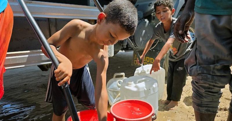 فلسطينيون يملئون خزانات المياه من شاحنة توزيع في مخيم للنازحين